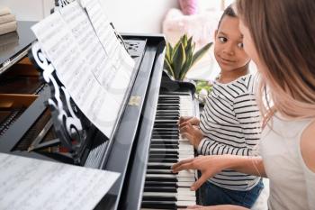 Woman teaching little African-American boy to play piano at home�