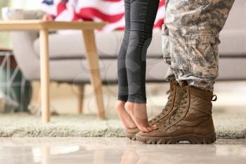 Girl standing on feet of her military father at home�