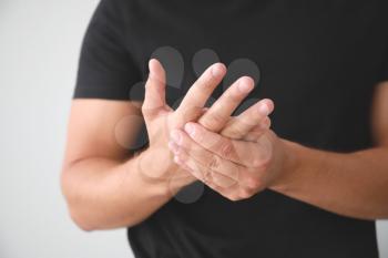 Young man suffering from pain in wrist on light background, closeup�