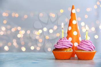 Tasty Birthday cupcakes and party hat on table against defocused lights�