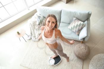 Happy young woman on scales at home. Weight loss concept�