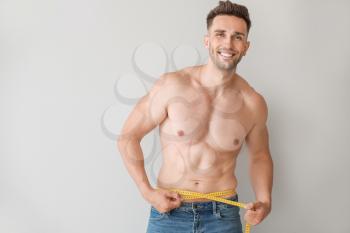 Handsome muscular man with measuring tape on light background. Weight loss concept�