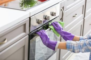 Woman cleaning oven in kitchen�