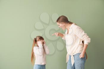 Angry mother scolding her little daughter on color background 