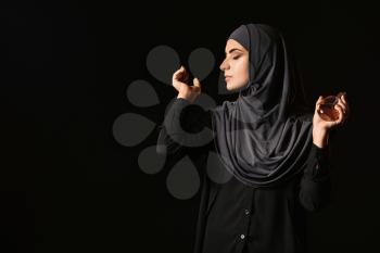 Beautiful Muslim woman with perfume on dark background�