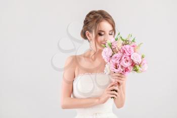 Portrait of beautiful young bride with wedding bouquet on light background 