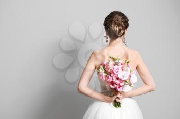 Beautiful young bride with wedding bouquet on grey background,  back view�