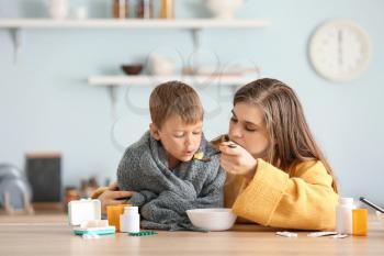 Mother feeding her sick son with chicken soup in kitchen�