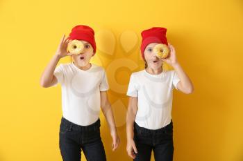 Portrait of surprised twin girls with tasty donuts on color background�