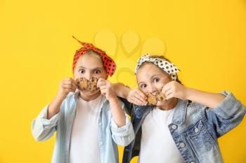 Portrait of funny twin girls with cookies on color background�