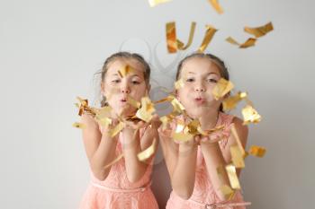 Portrait of cute twin girls blowing confetti on light background�
