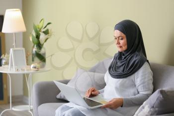 Beautiful mature Muslim woman with laptop at home�