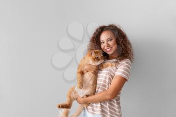 Young African-American woman with cute cat on light background�