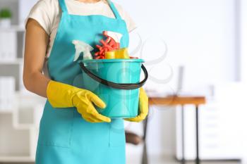 Female janitor with set of cleaning supplies in office�
