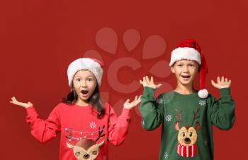 Cute children in Christmas sweaters and Santa hats on color background�