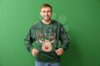 Young man in Christmas sweater on color background�