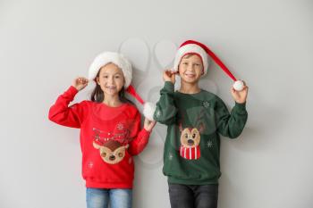 Funny children in Christmas sweaters and Santa hats on light background�