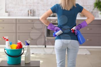 Woman with set of cleaning supplies in kitchen�