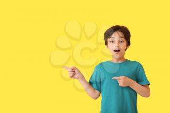 Surprised little boy pointing at something on color background�