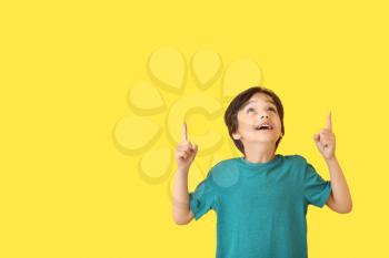 Happy little boy pointing at something on color background�