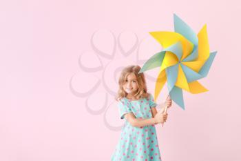 Cute little girl with paper windmill on color background�