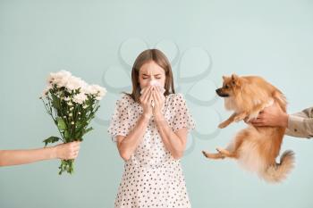 People giving flowers and dog to young woman suffering from allergy on light background�