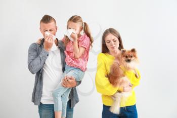 Young woman with dog and husband with daughter suffering from pet allergy on light background�