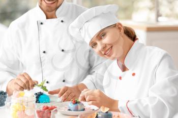 Young confectioners decorating tasty dessert in kitchen�