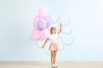 Little girl with balloons pointing at something near color wall�