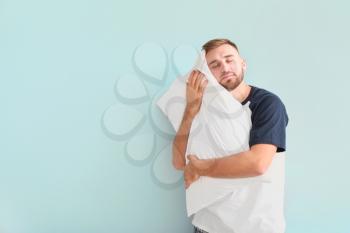 Sleepy young man with pillow on light background�