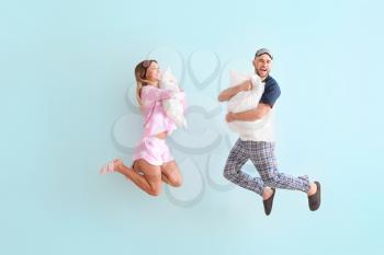 Jumping young couple with pillows on color background�