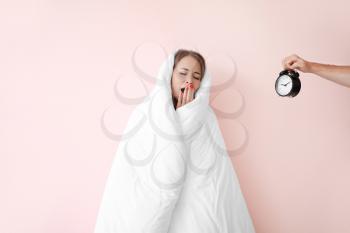 Sleepy young woman wrapped in blanket and male hand with alarm clock on color background�