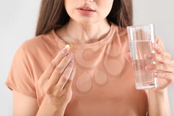 Young woman taking pill on light background, closeup�