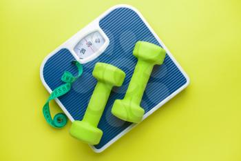 Scales, dumbbells and measuring tape on color background. Weight loss concept�