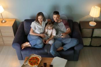 Happy family eating pizza while watching TV at home�