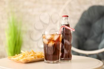 Glass, bottle of cold cola and french fries on table�