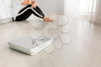 Scales and depressed young woman in room. Weight loss concept�