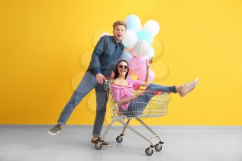 Young couple with shopping cart and balloons near color wall�