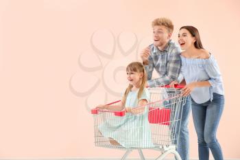 Surprised family with shopping cart on color background�