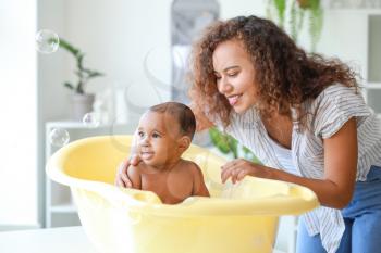 Young African-American mother washing her baby at home�