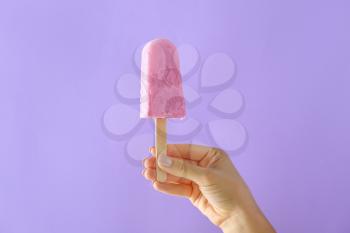 Female hand with tasty blueberry ice cream on color background�