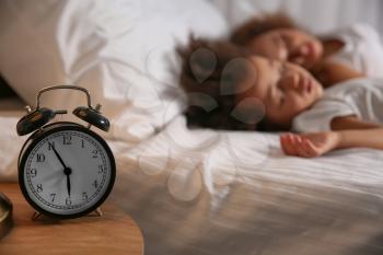 Sleeping African-American girl with mother and alarm clock on table�