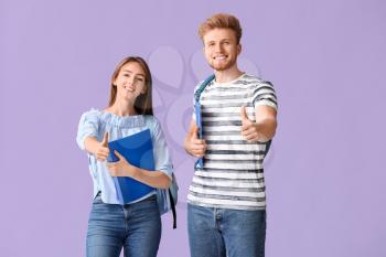 Portrait of female and male students showing thumb-up gesture on color background�