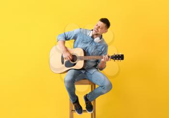 Handsome man playing guitar on color background�