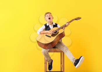 Little boy playing guitar and singing on color background�