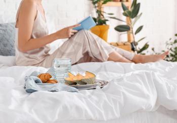 Tray with tasty breakfast and woman reading book on bed�