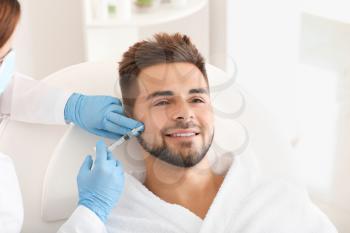 Handsome man receiving filler injection in beauty salon�