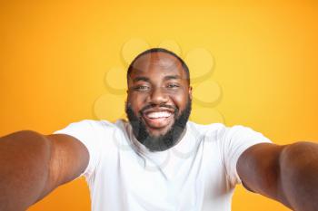 Happy African-American man taking selfie on color background�