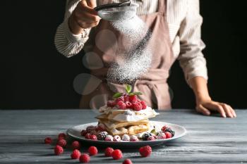Woman sprinkling sugar powder onto Belgian wafers on table�