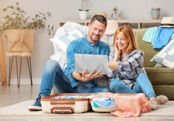 Couple with laptop and luggage planning their vacation at home�